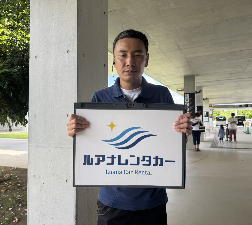 A Luana Rent a Car staff member holding the company sign at Miyako Airport